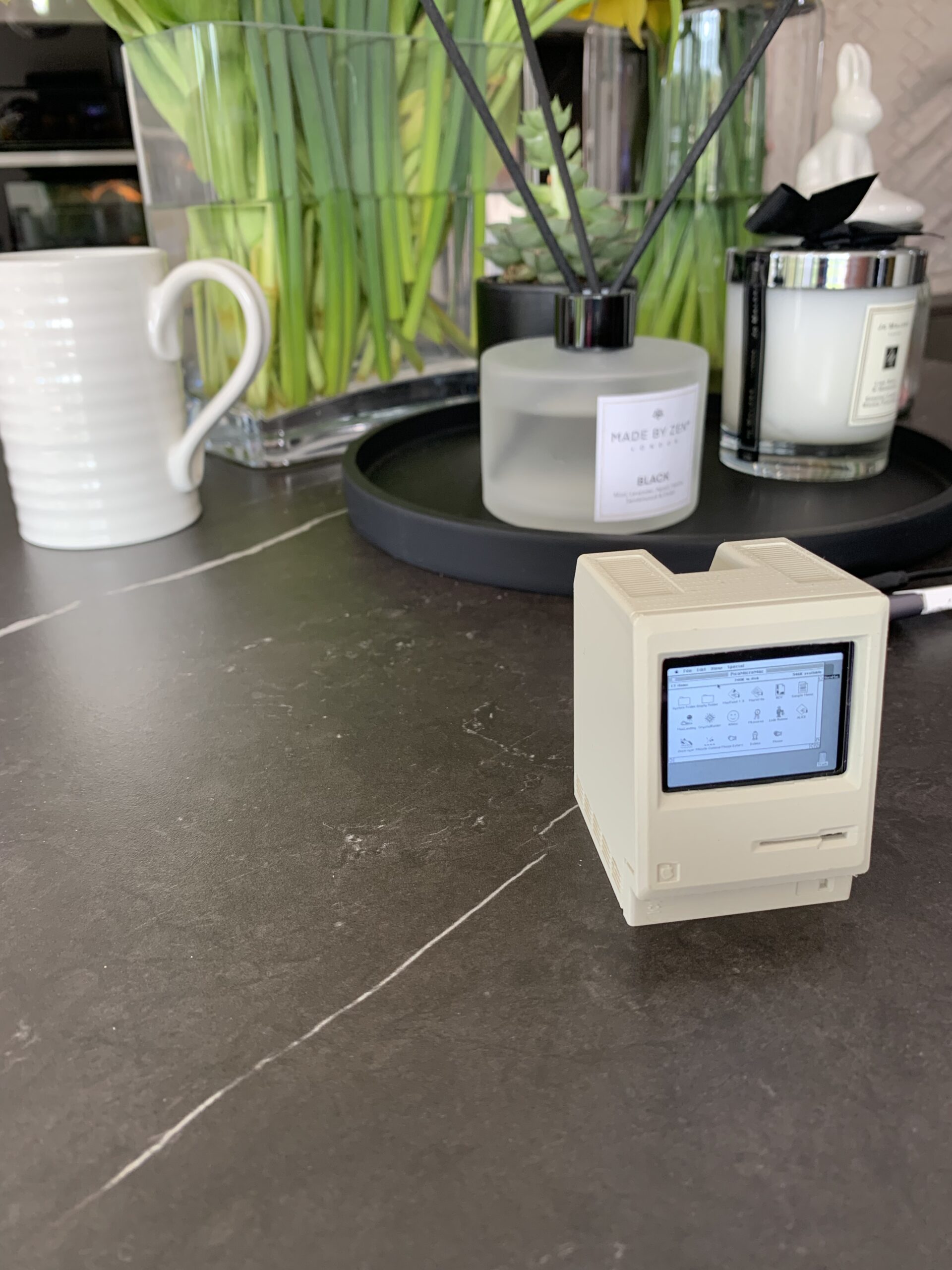 The Pico-mac-nano desktop on a table, with diffuser, candle, and a coffee mug for scale.