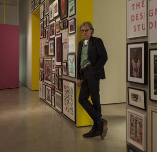 Paul Smith leaning on a yellow painted wall next to his framed art