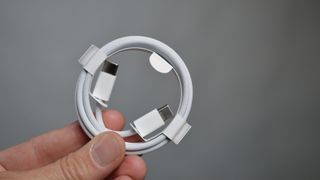 iPhone 15:n valkoinen latauskaapeli ihmisen kädessä harmaata taustaa vasten