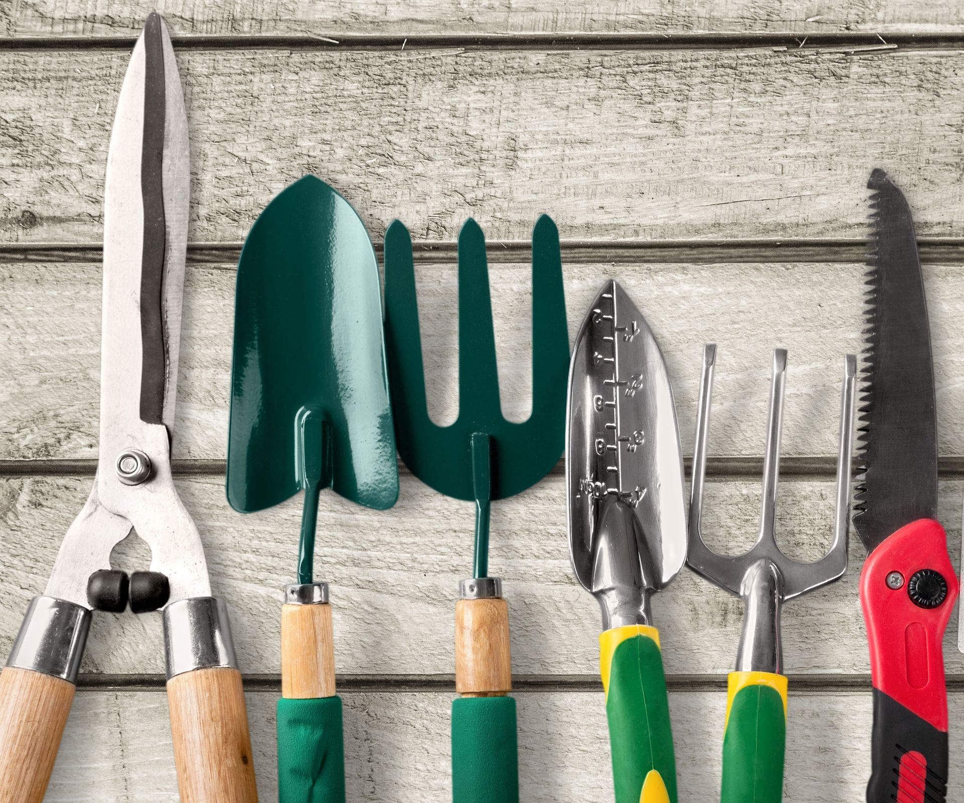 mixed gardening tools on pale wooden surface