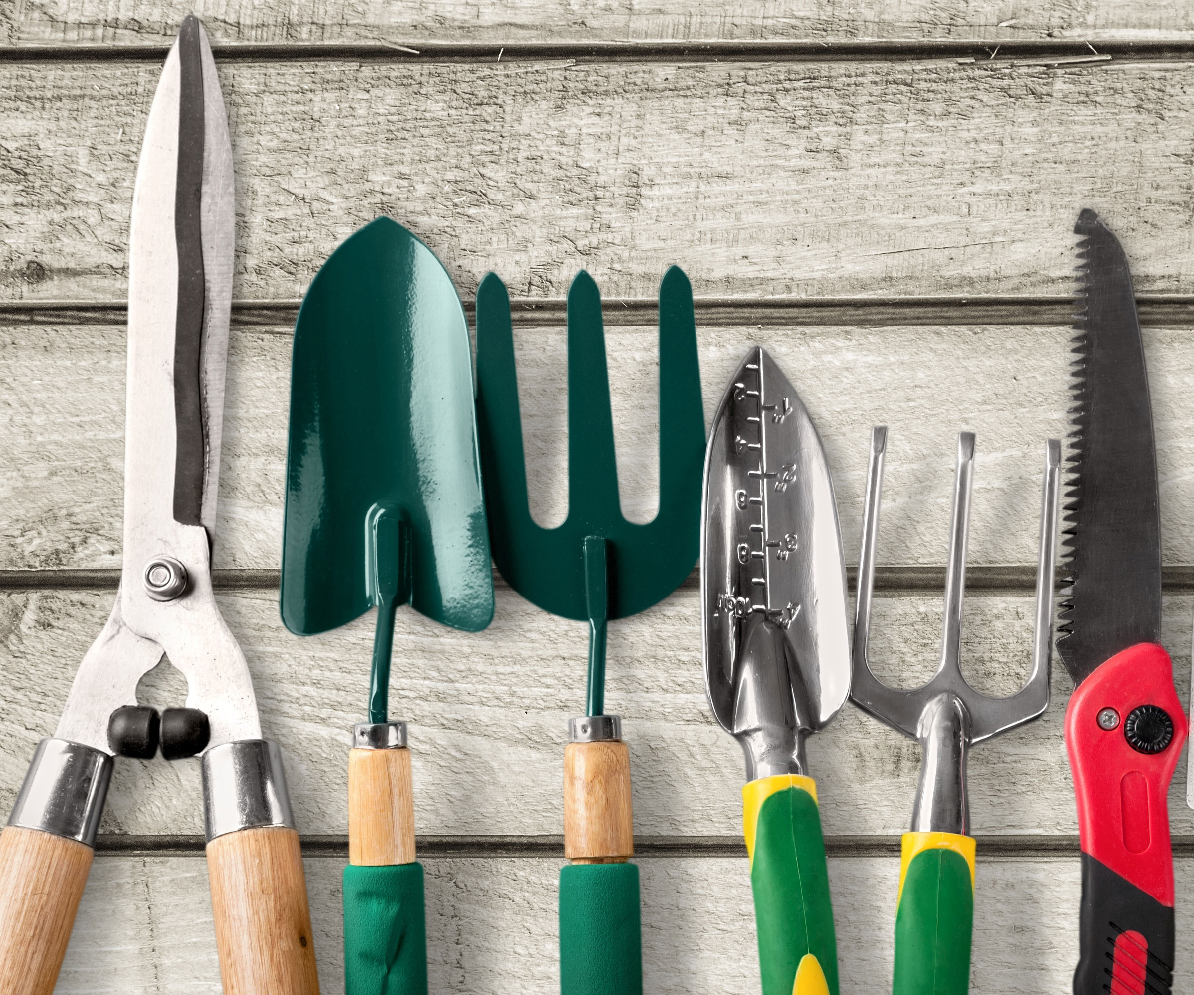mixed gardening tools on pale wooden surface