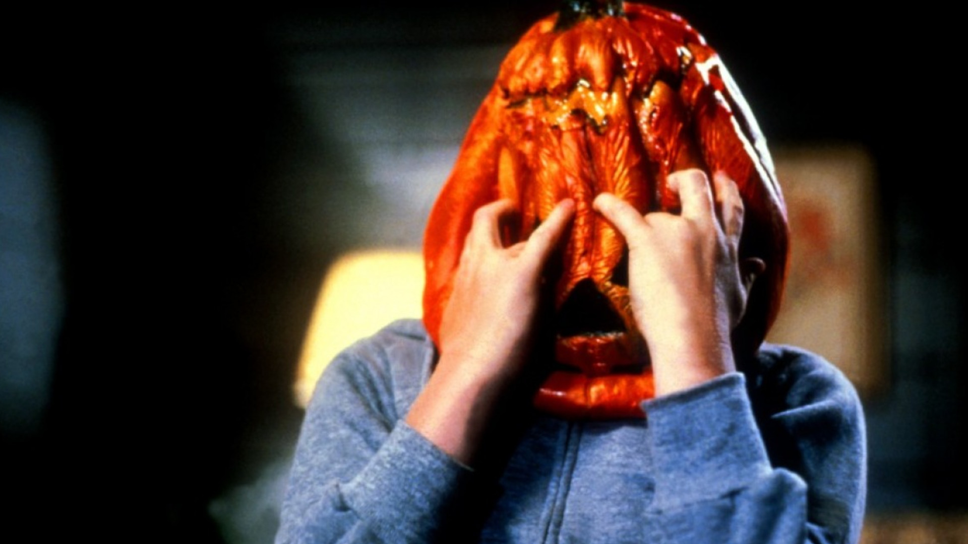 A young boy clawing at a pumpkin mask that he is wearing during Halloween 3: Season of the Witch.