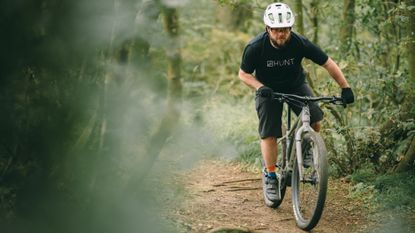 Tech Writer Matt riding a prototype Cairn Brave electric gravel bike in some woods.