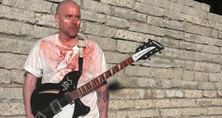 Evil Island guitarist Cody Votolato is covered in theatrical blood and pictured against a wall with his black Rickenbacker.