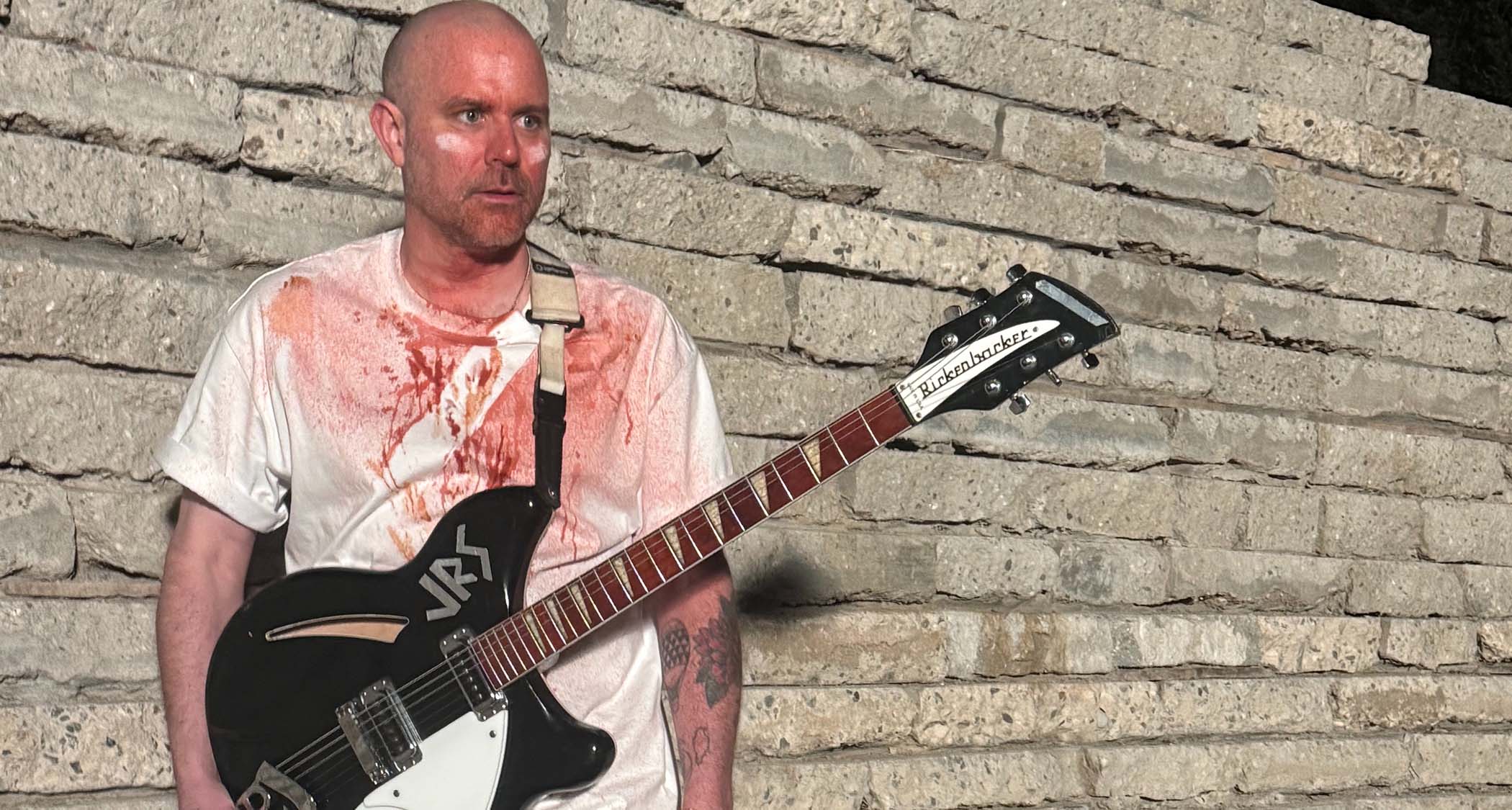 Evil Island guitarist Cody Votolato is covered in theatrical blood and pictured against a wall with his black Rickenbacker.