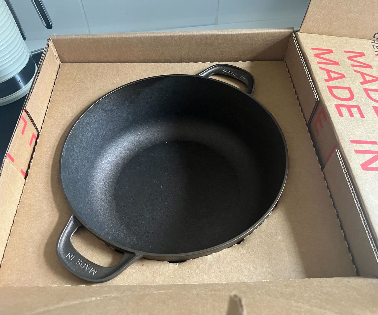 A Made In cookware cardboard box on a black kitchen counter with a Dutch oven inside.
