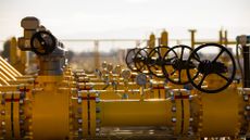A close-up photo of a natural gas pipeline, shot in the day in a wide open space with multiple yellow pipes visible one in front of another.