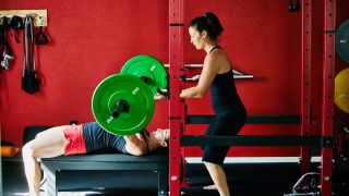 Woman presses heavy barbell with spotter