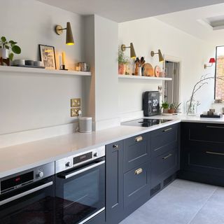 Charcoal grey kitchen with white worktops and upstands and an open shelf running along the wall