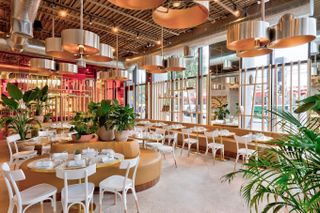 A modern glamour-inspired café features round golden chandeliers, white wooden tables and chairs, and coffee-hued upholstered banquettes.