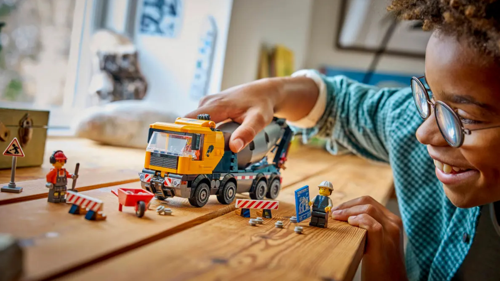 A child smiles while playing with Lego Cement Mixer set on a wooden table