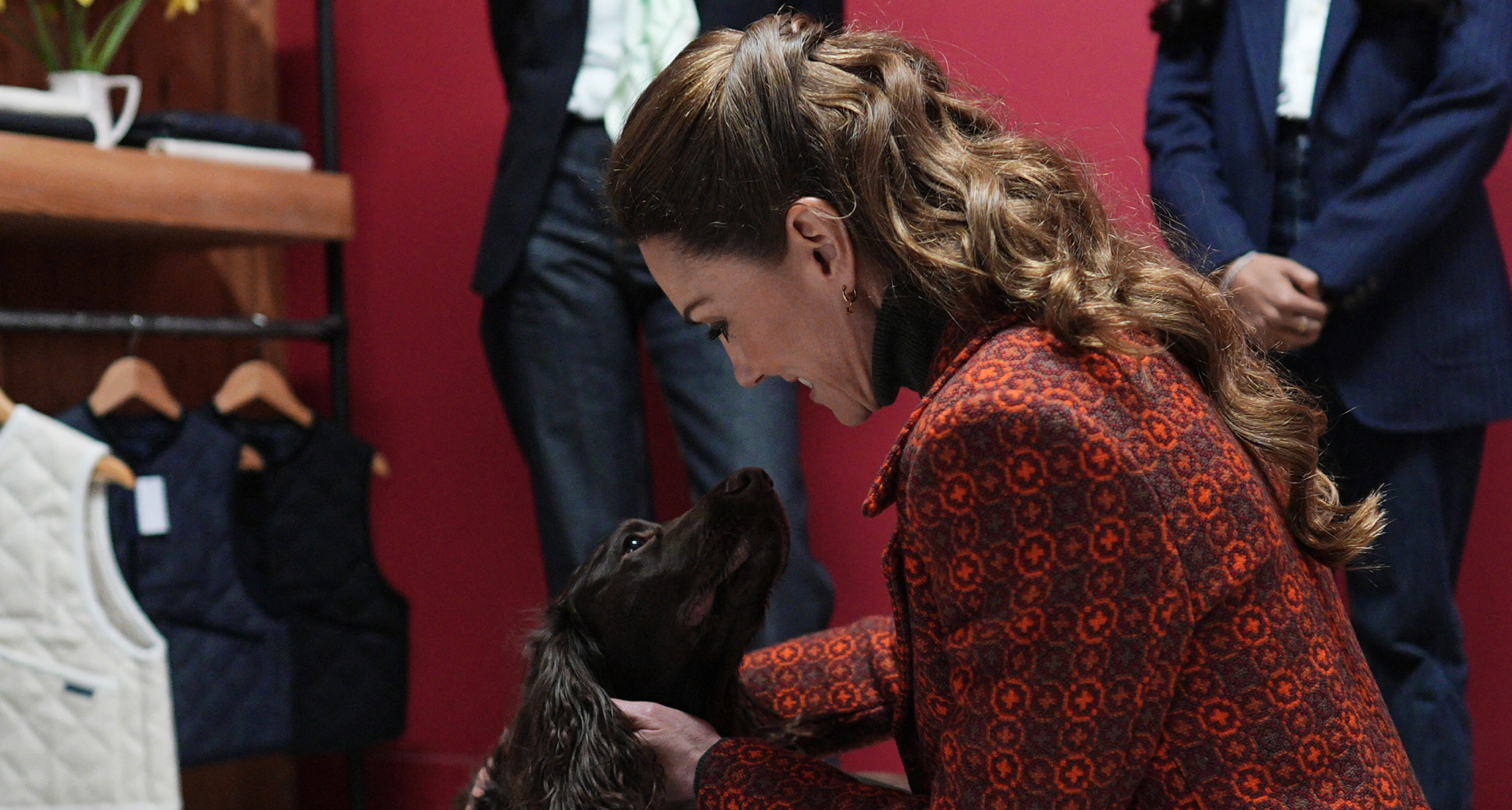 Princess Kate wearing an orange coat petting a black dog 