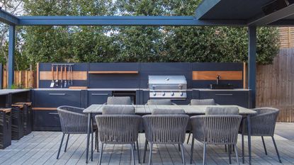 A. grey outdoor kitchen/living area with wooden countertops and a gas grill