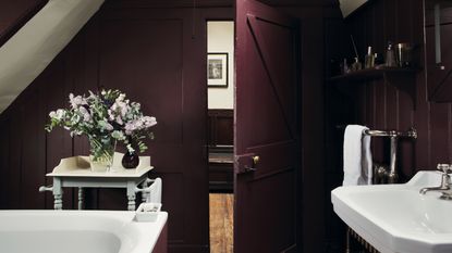 Plum bathroom with painted walls and door, hint of bath to the left, vintage cabinet with vase of flowers 