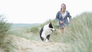 Woman smiling walking dog on sand dune