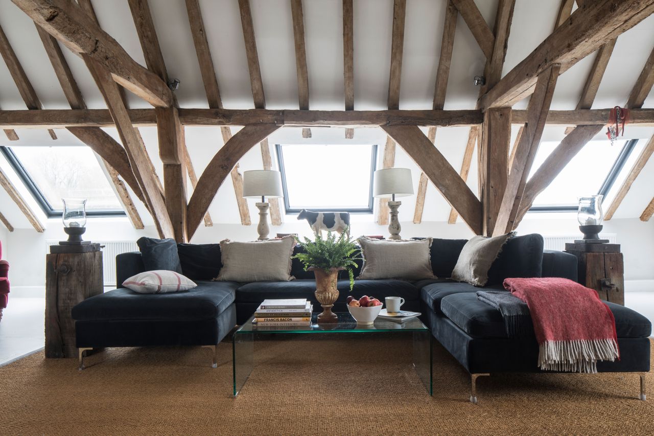 living room with blue velvet modular sofa and glass coffee table and sisal rug with vaulted ceiling and rooflightswhite walls with beams