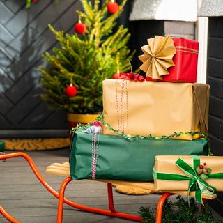 an orange wire sleigh with red, green and gold wrapped presents on top, sitting on black porch