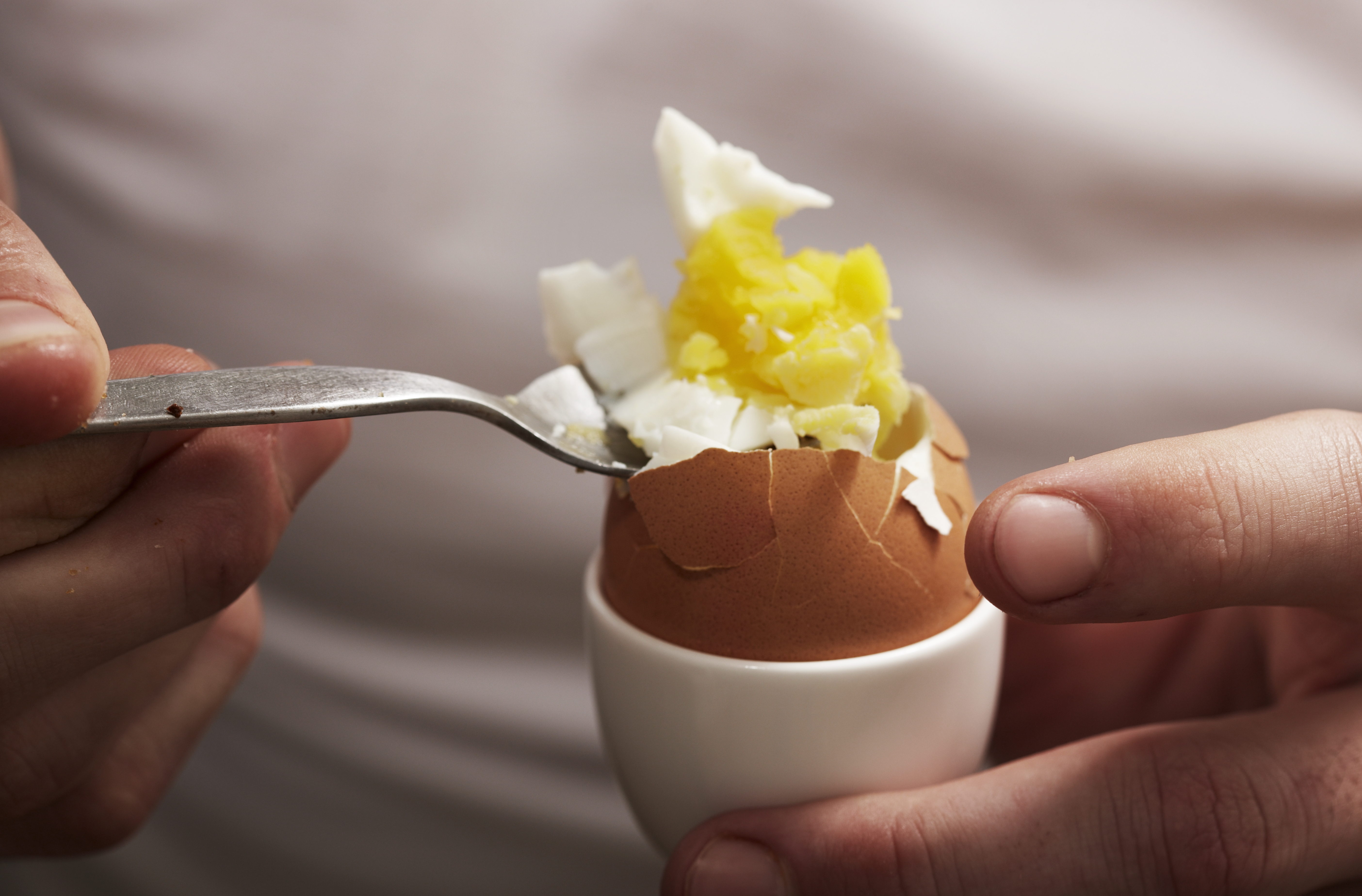 Close up image of a person using a fork to scoop out the insides of a hard-boiled egg.