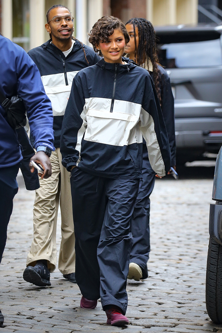Zendaya wearing a navy and white windbreaker jacket, navy pants, and burgundy sneakers.