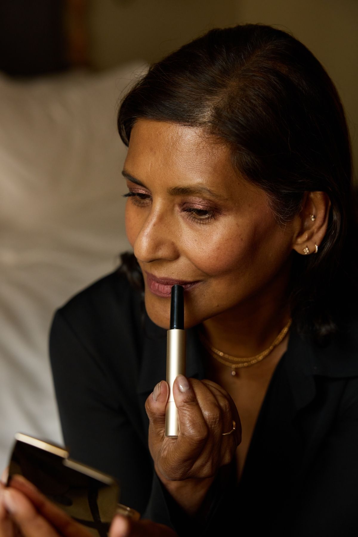 Ruby Hammer MBE applying the Hourglass Phantom Blur Balm on her lips whilst looking into a compact mirror