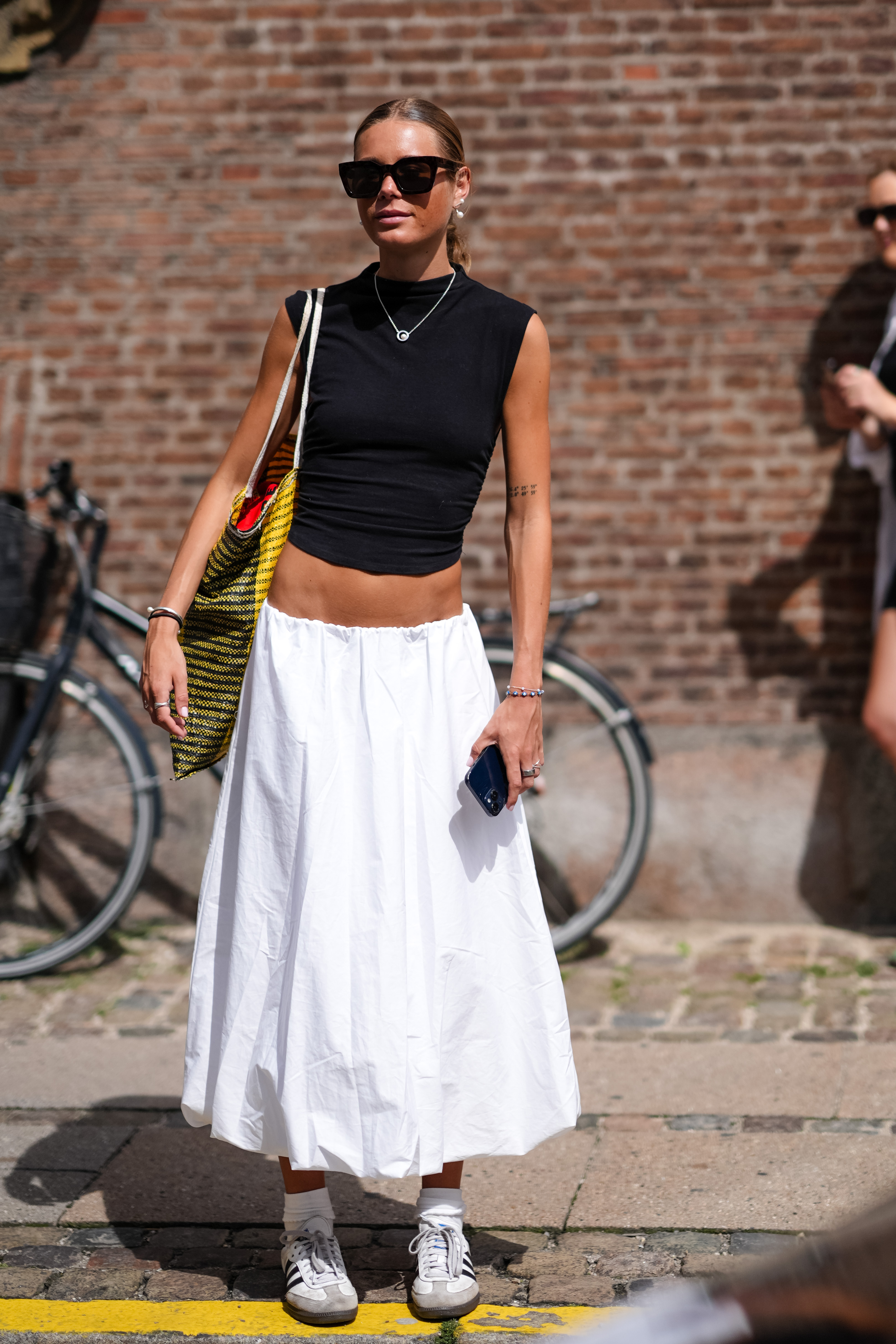woman wearing black top, white skirt, and adidas sambas