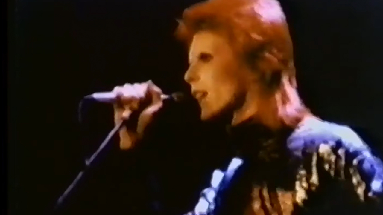 David Bowie singing into a microphone with a mullet