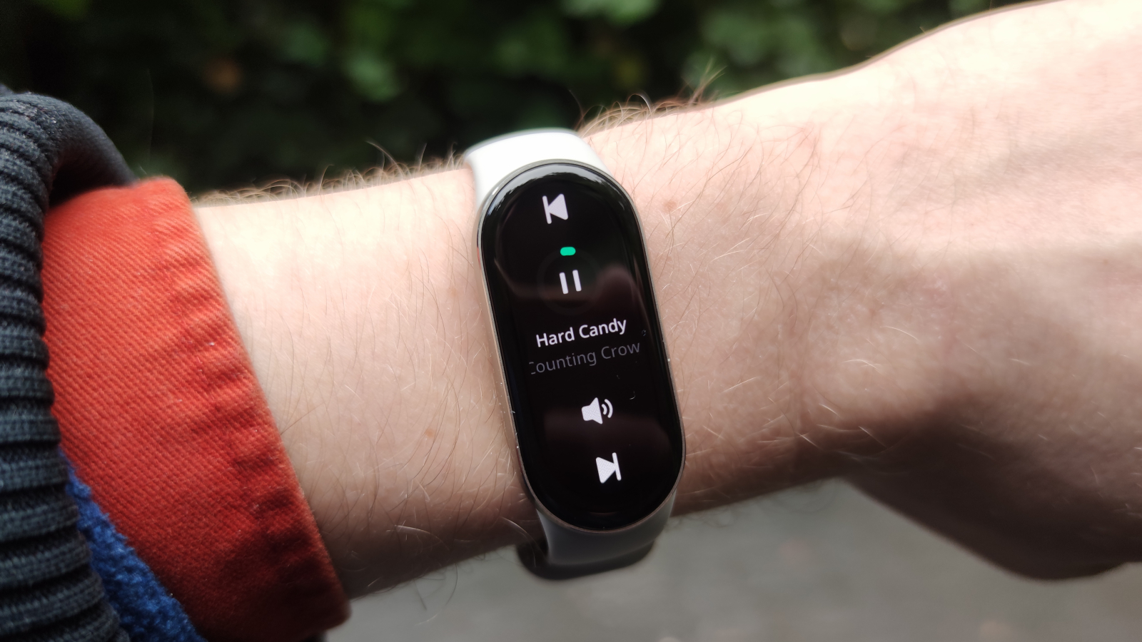 The Xiaomi Smart Band 9 on a man's wrist in front of a green park.