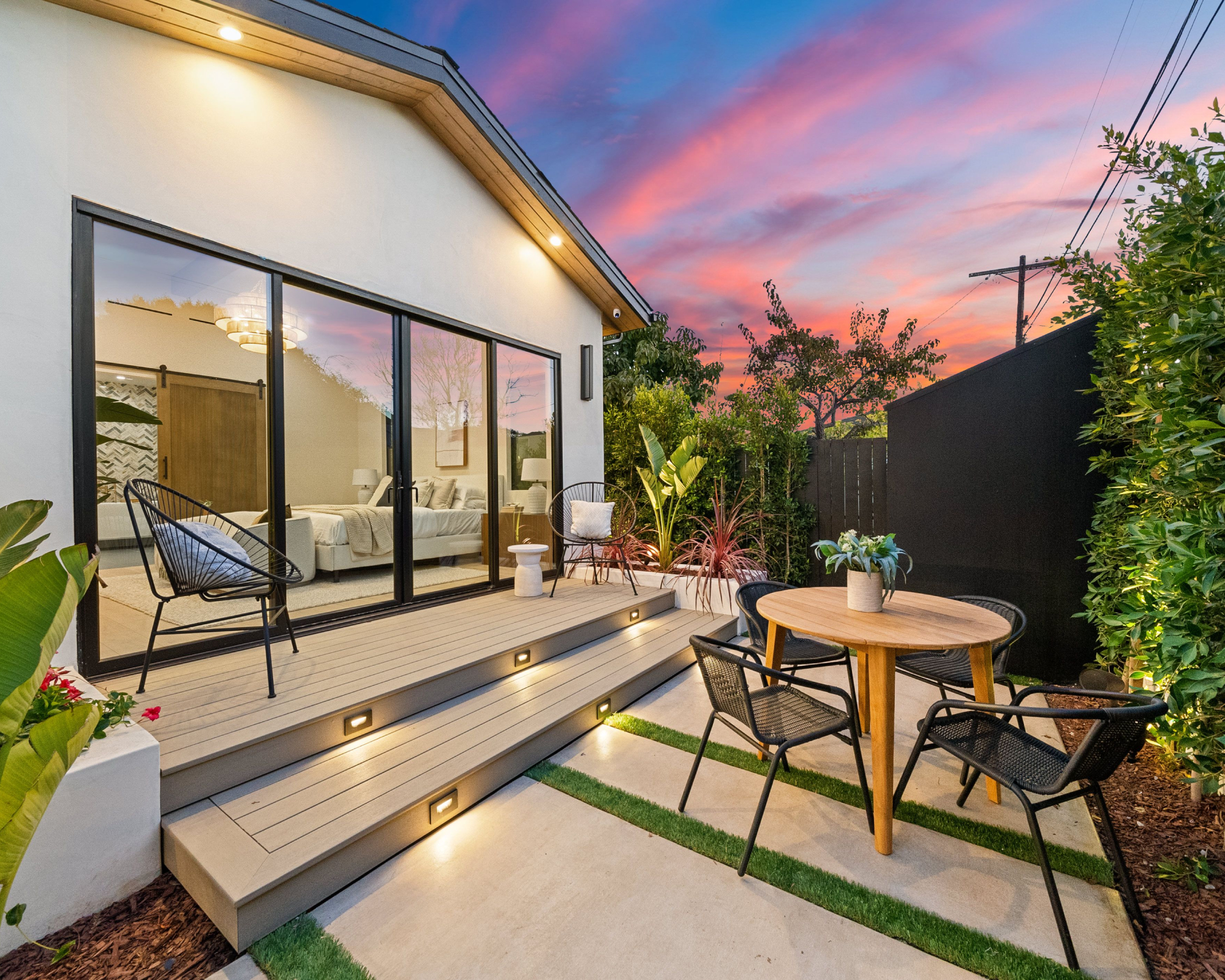 Modern patio with stylish furniture and plants at sunset, featuring a cozy outdoor seating area and glass doors leading indoors.