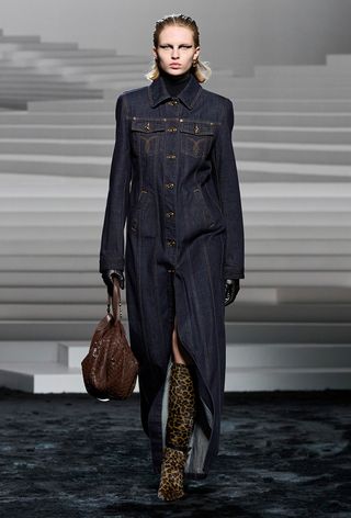 animal print boot trend is shown on the fall winter 2025 runway show of Versace with a model wearing a denim maxi dress with leopard print knee-high boots and a brown bag