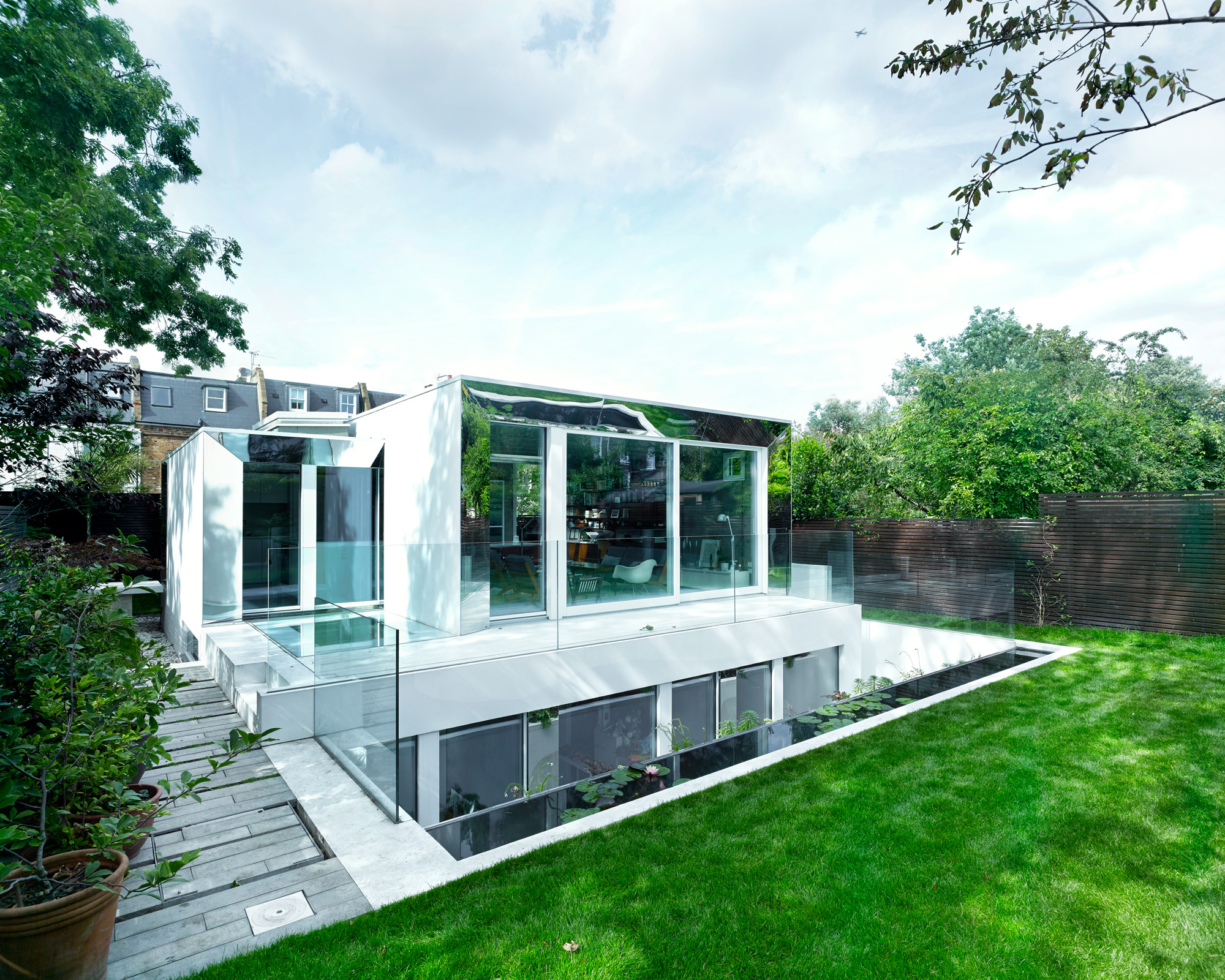 A building which sinks to below ground level is surrounded by grass and trees, with large glass panels making up the walls so that the furniture inside is visible.