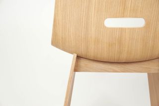 A close-up of a wood chair with a curved edge rectangle hole in the back.