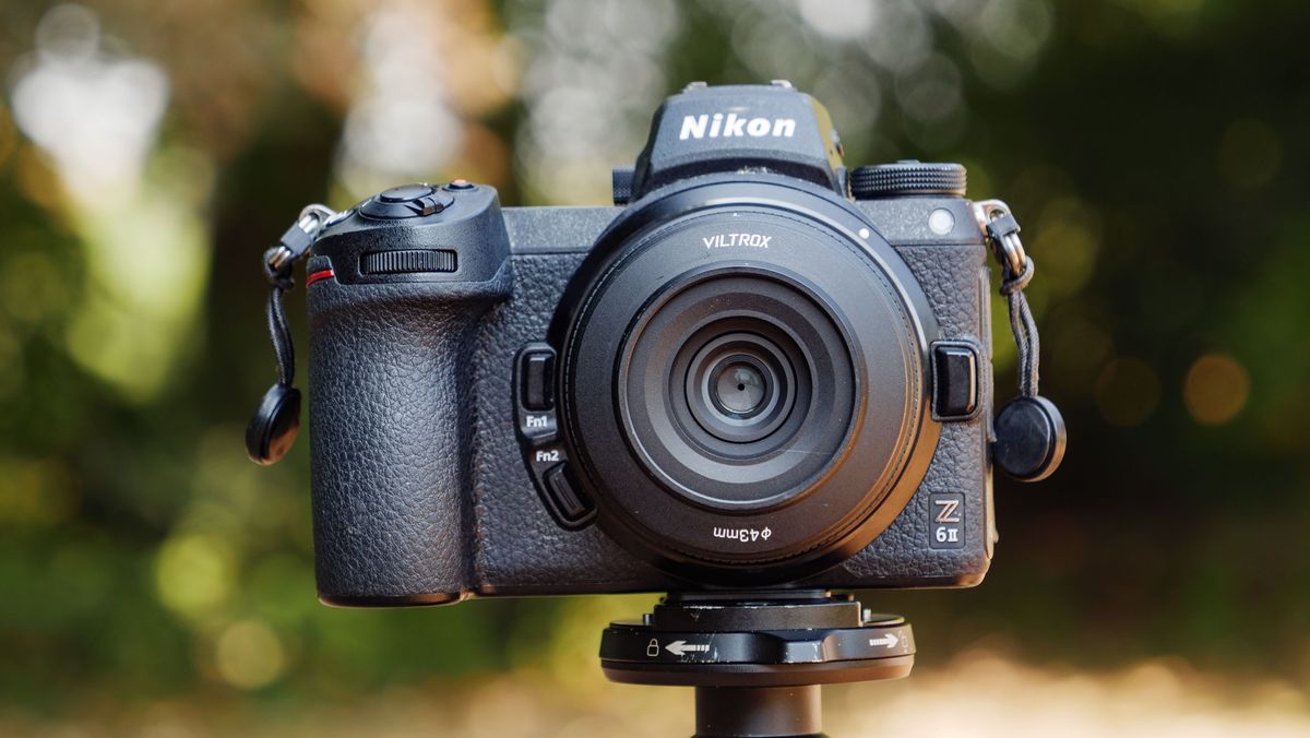 Viltrox AF 26mm F2.8 EVO 'pancake' lens attached to a Nikon mirrorless camera, there's dappled light through a tree behind it. Lens filter accessory is attached