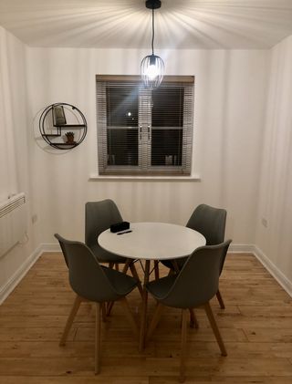 A small white room with blank walls and a small round table and chairs in the middle.