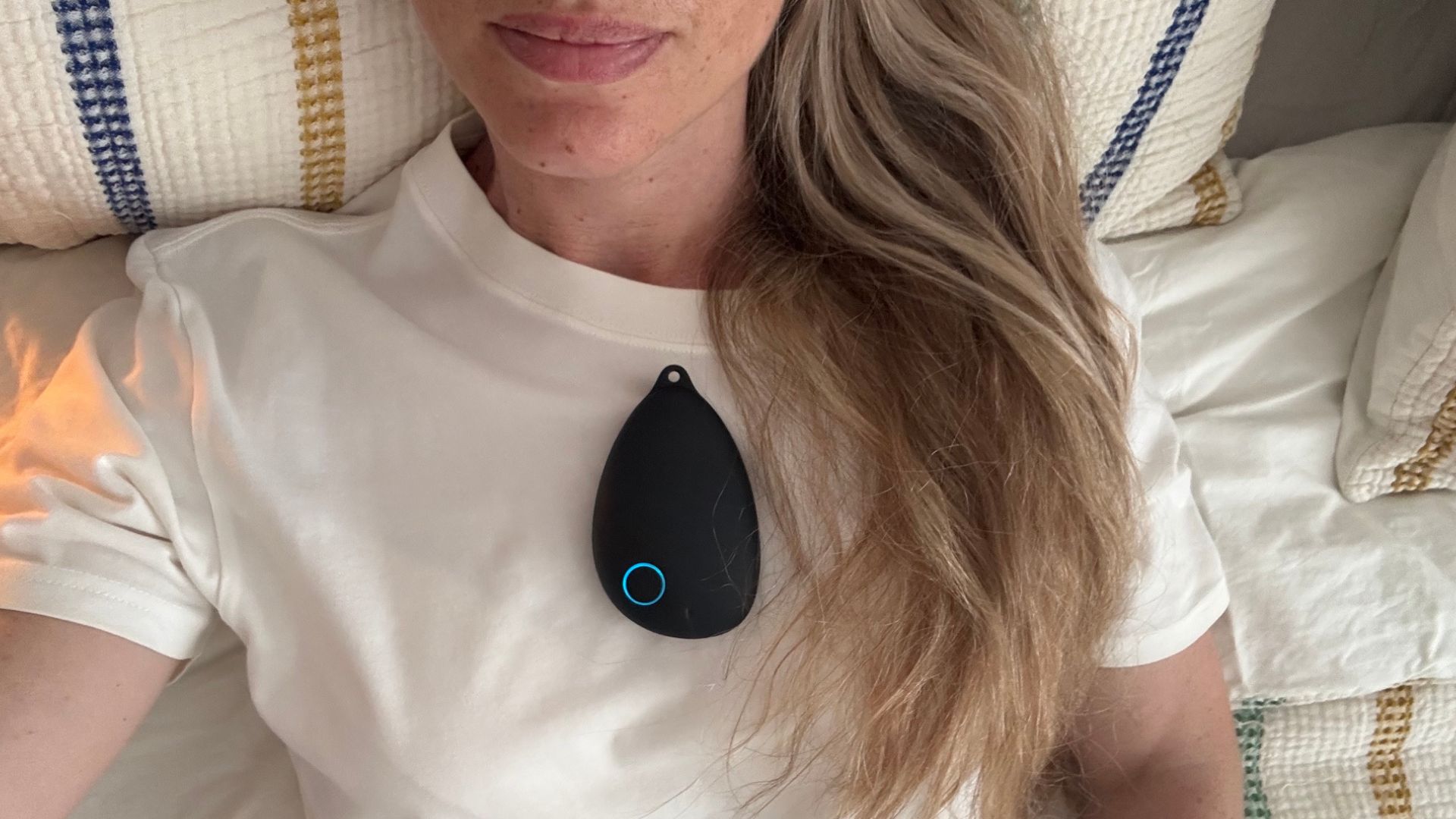The image shows a blonde sleep writer lying in bed with a pebble-shaped object resting on her sternum