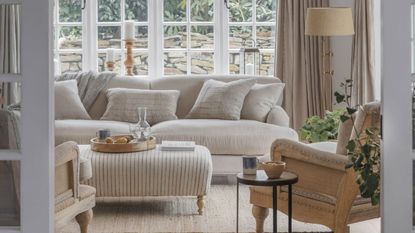 A neutral living room with a puffy cream sofa, ottoman table, and two arm chairs