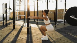 Woman outdoors in outside gym performing a bodyweight squat with arms outstretched
