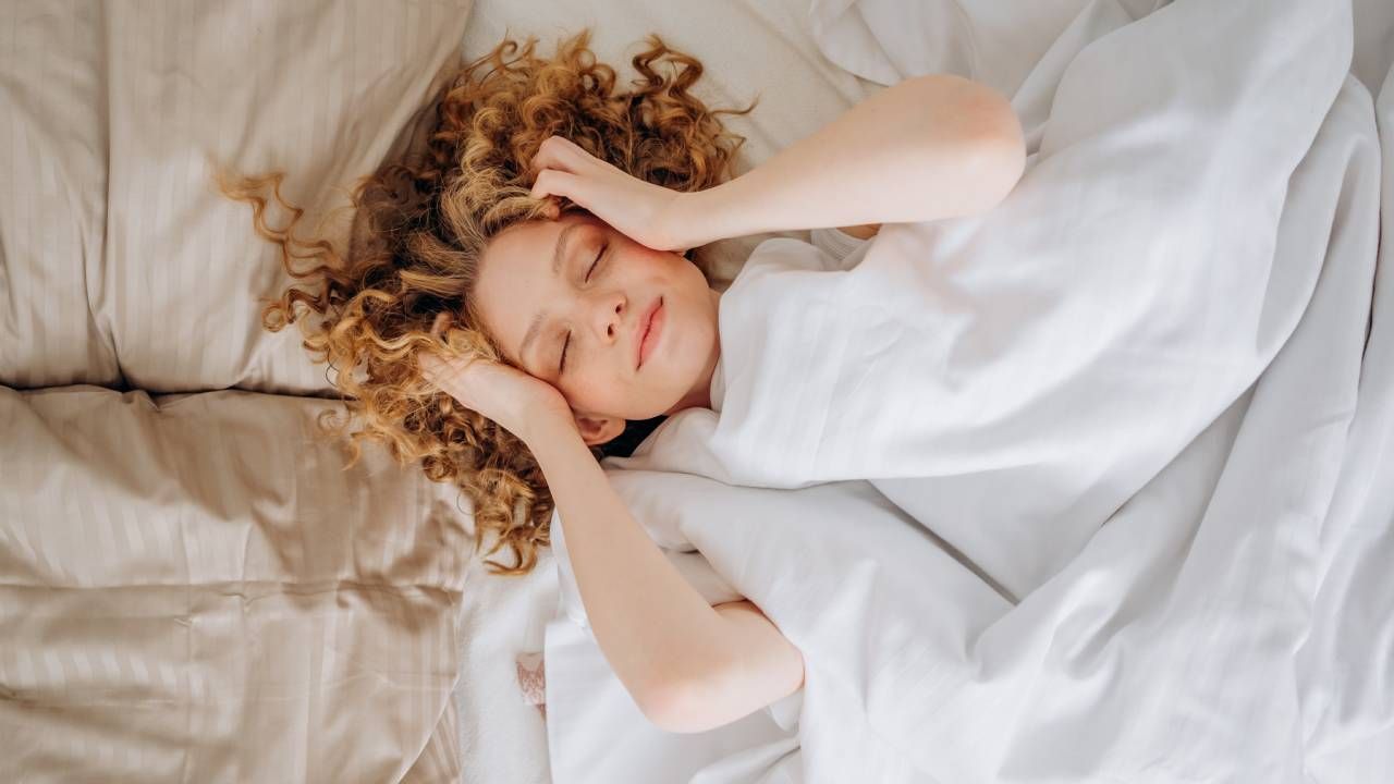 Best sleep temperature, curly haired woman sleeping under a cosy duvet