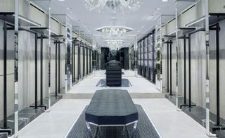 A hallway with marble floors, a blue fabric covered bench, blue shelves and crystal chandeliers.