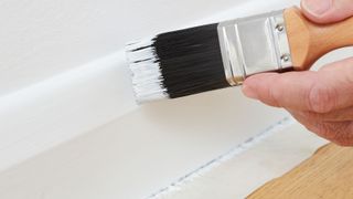 Painting skirting board with a brush and masking tape