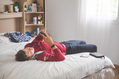 Cyclist dressed in casual clothes lying on bed reading from their smartphone