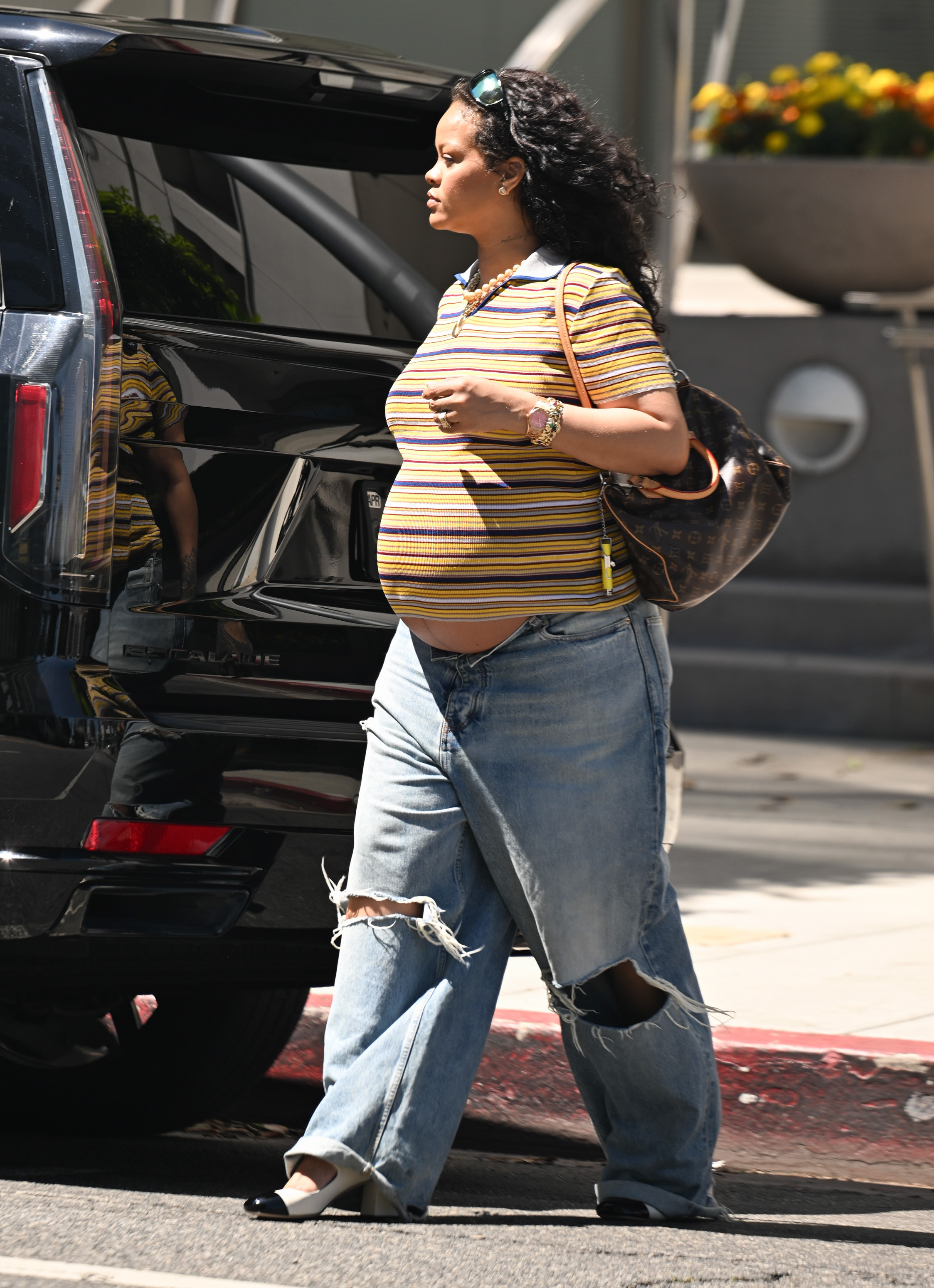 Rihanna styled ripped light-wash jeans with a striped polo shirt and a Louis Vuitton bag