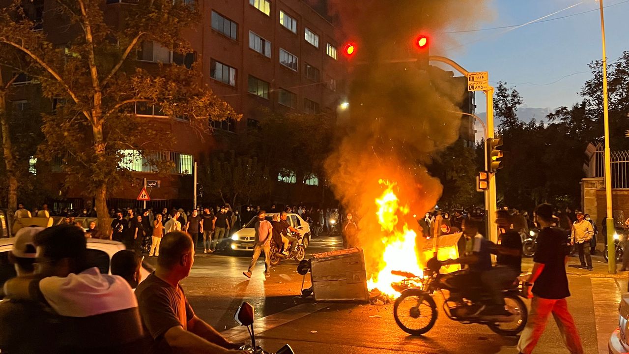 An angry crowd gathers around a burning barricade during a protest for Mahsa Amini