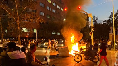 An angry crowd gathers around a burning barricade during a protest for Mahsa Amini