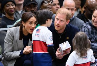 Prince Harry wearing a blue sweater talking to a little boy holding a Prince Harry Funko Pop