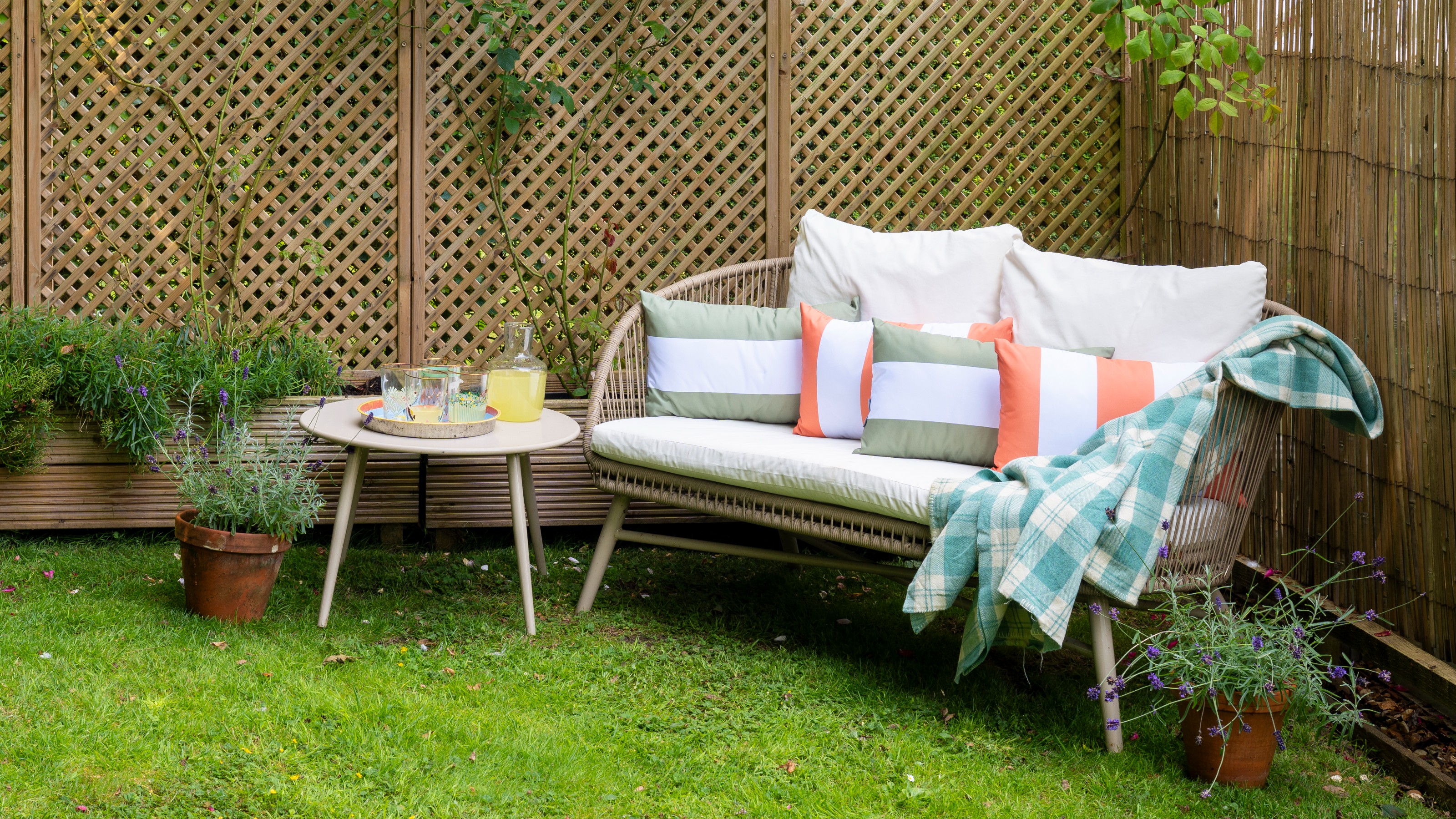 A garden with a small outdoor sofa with striped cushions and a side table