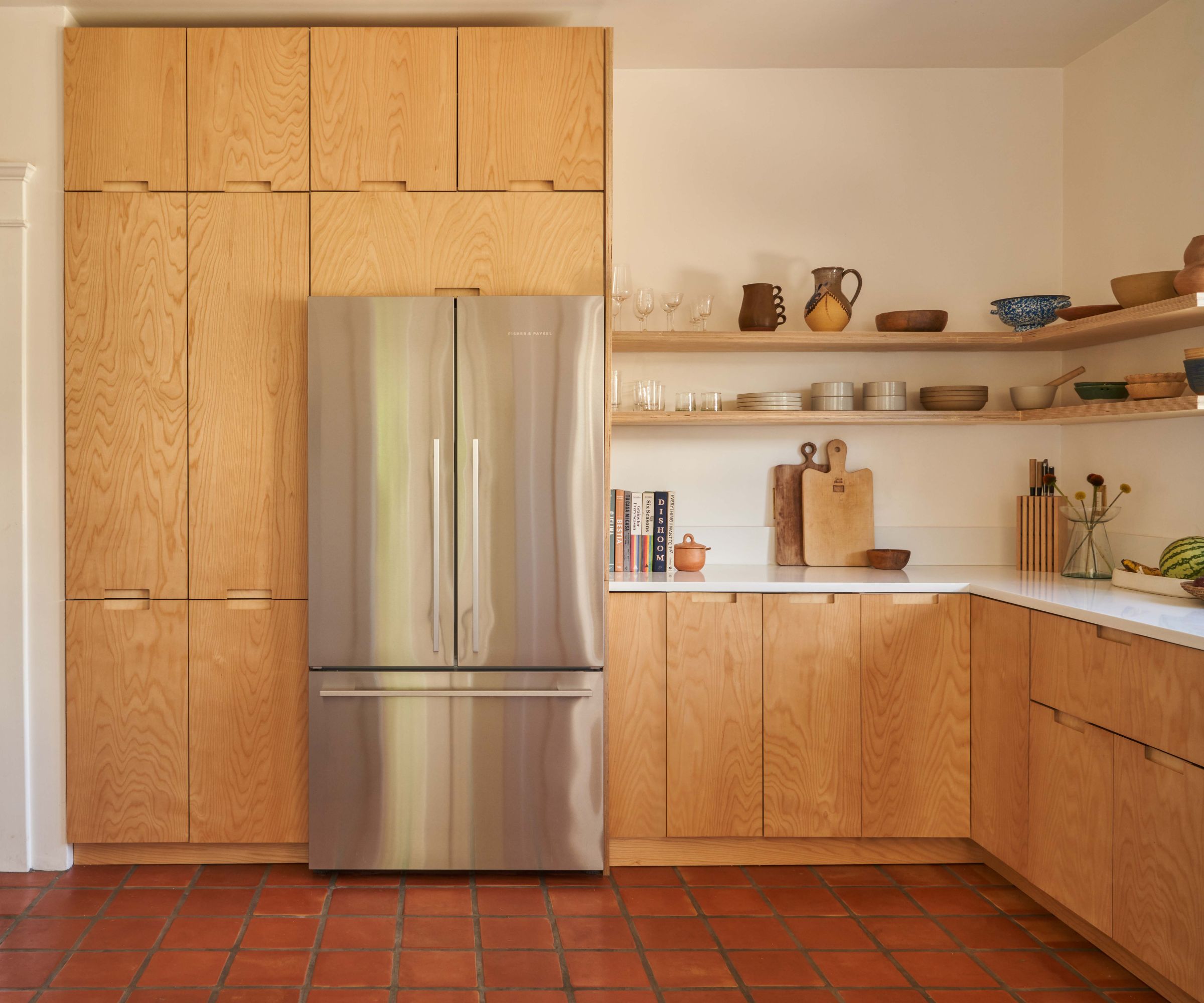 Modern kitchen wall featuring floor-to-ceiling wood storage, a stainless steel French door refrigerator, and terracotta tile flooring.