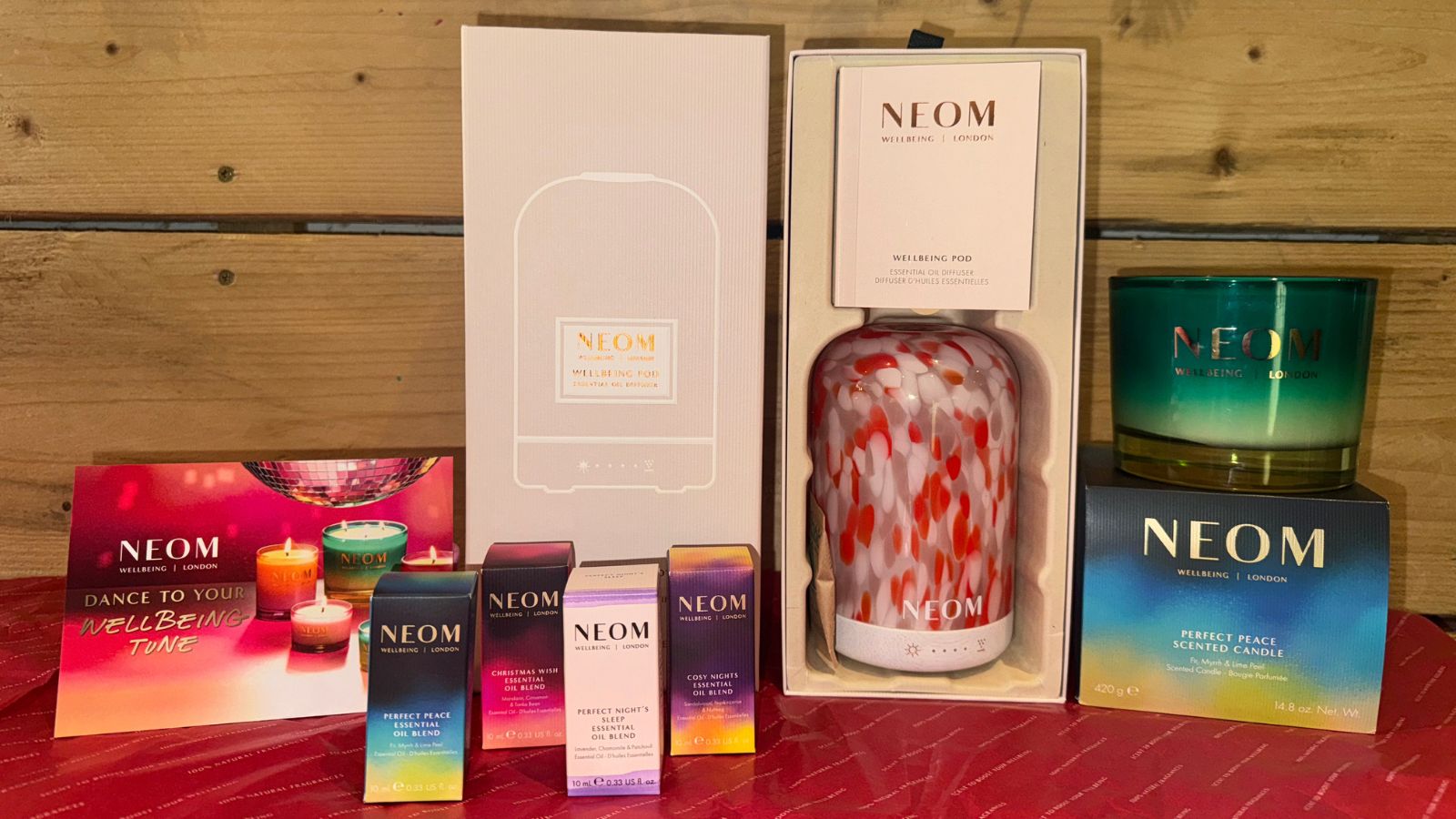 Arrangement of NEOM products including the pink Clementine Wellbeing Pod in box next to boxed essential oil blends and a green candle
