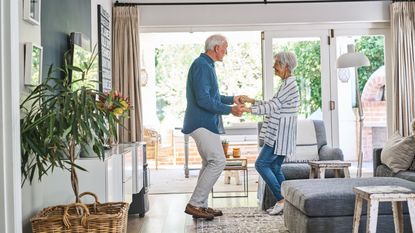 A happy older couple dance in their living room.