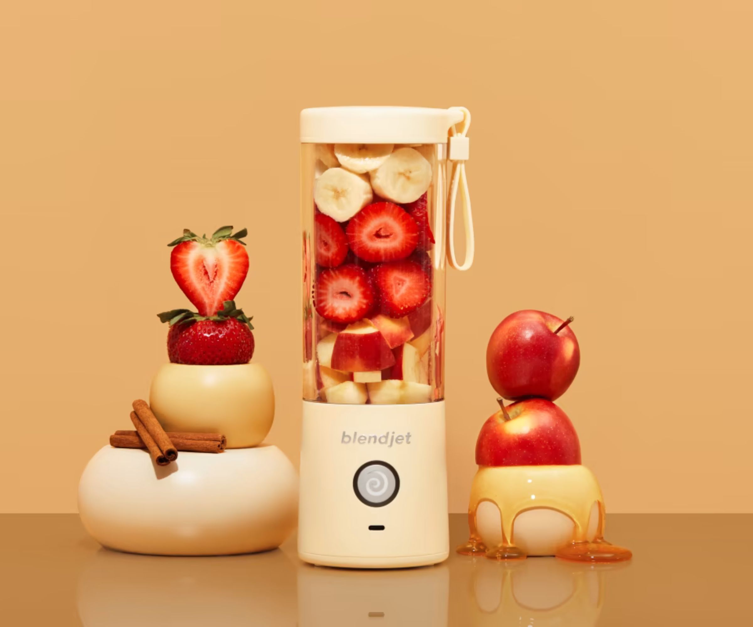 A BlendJet Portable Blender against a gold background, surrounded by soft fruits.