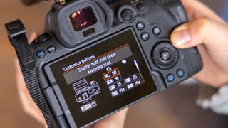 Person holding a Canon camera, with the Customize buttons screen displaying the shutter button